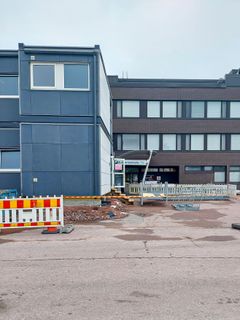 Rakennustyömaa kaksikerroksisen liiketalon edustalla, esteaita ja keskeneräistä maatyötä.