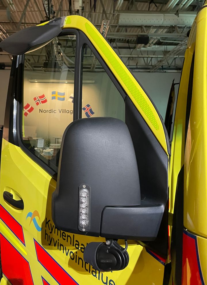 Ambulanssin sivupeili Nordic Villagessa, taustalla Pohjoismaiden lippuja.