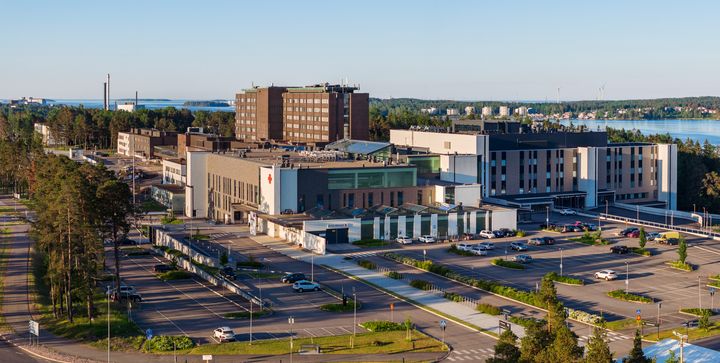 Ilmakuva suuresta sairaalarakennuksesta vehreässä ympäristössä lähellä vesistöä.