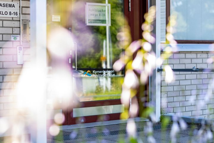 Tiiliseinä ja ovi, joissa Kymenlaakson hyvinvointialueen logo.