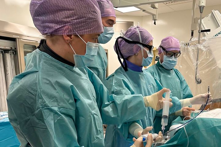 Lääkäritiimi leikkaussalissa. Kaikilla on yllään leikkausvaatteet, maskit ja käsineet.