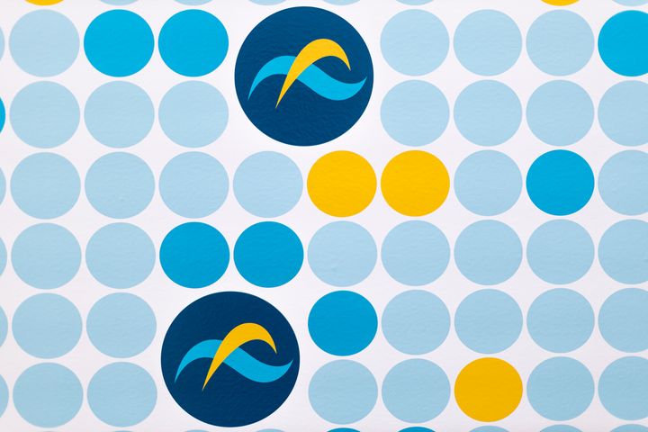 Sinisiä ja keltaisia ympyröitä muodostavat kuvion valkoisella taustalla. Kaksi suurta tummansinistä ympyrää sisältävät aalto- ja kaarikuviot.