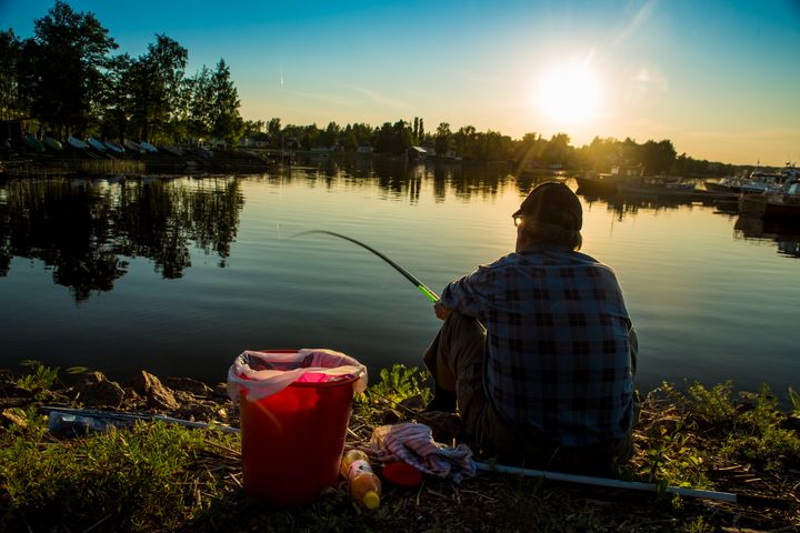 Henkilö istuu järven rannalla auringonlaskussa kalastamassa.