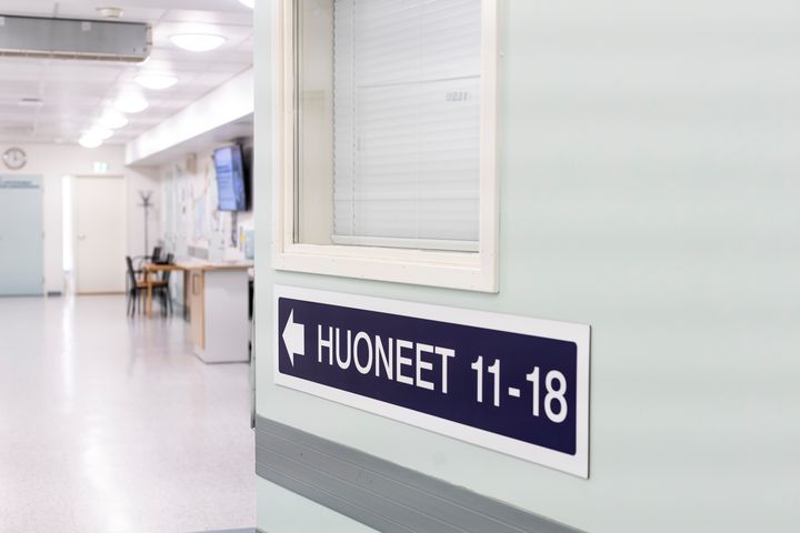 Sininen opastekyltti "Huoneet 11-18" nuolella vasemmalle, terveysaseman käytävällä.