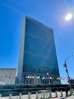 pilvenpiirtäjä, jonka edessä eri maiden lippuja, taustalla sininen taivas