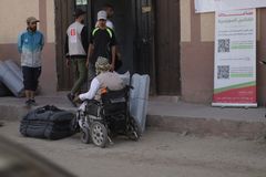 Henkilö pyörätuolissa odottaa majoitustarvikkeiden jakoa Gazassa. Taustalla rakennus ja muutama henkilö.