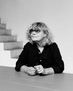 Marie-José Van Hee istuu pöydän ääressä. Taustalla portaat, jotka ovat hänen arkkitehtuurilleen tunnusomaiset.