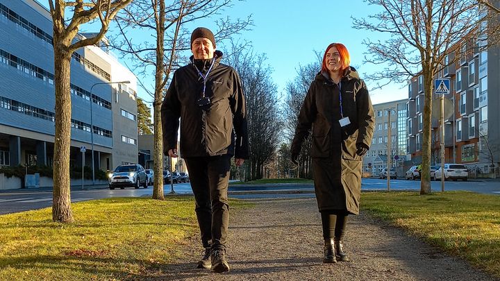 Kaksi ihmistä kävelee puistikkoa rinnakkain