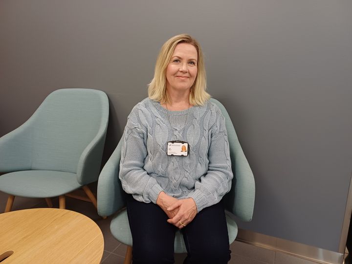 En blond Sari West sitter på en stol och ler.