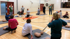 Opettajat harjoittelevat elvytystaitoja liikuntasalissa nukkejen avulla.