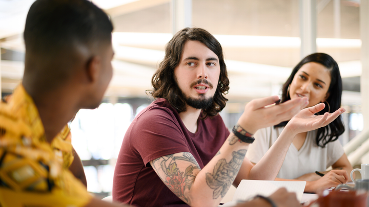 Kolme ihmistä keskustelee pöydän äärellä toimistoympäristössä.