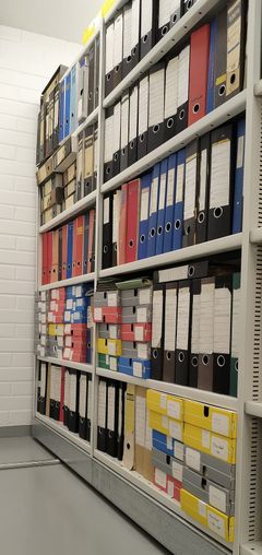 Kuva arkistohyllyistä täynnä eri värisiä kansioita.