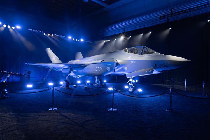 Kuvassa on F-35-hävittäjä roll out -tilaisuudessa. Taustalla on tummat valot ja hävittäjä on esillä näyttävästi valaistuna.