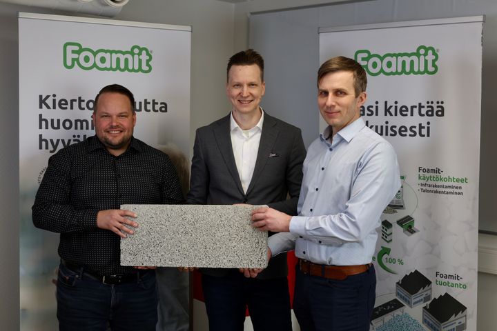 Kolme miestä pitelee uutta vaahtolasista valmistettua kattotuotetta kädessään Foamit Oyj:n tilaisuudessa. Taustalla on kaksi Foamit-logolla varustettua esittelytaulua.