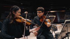 Kaksi viulistia harjoittelee yhdessä orkesterin harjoituksissa konserttisalissa.