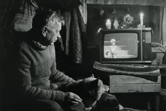 Vanha mies ja koira katsovat televisiota pimeässä huoneessa, jossa on kynttilöitä.