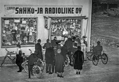 Mustavalkoinen kuva, jossa joukko ihmisiä katselee ulkona radiossa olevaa esitystä Sähkö- ja Radioliike Oy:n liikkeen ikkunan edessä. Talvinen maisema.