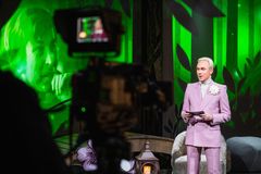 Kuvassa on juontaja Chistoffer Strandberg vaaleanpunaisessa puvussa studiossa, jossa on vihreitä valoja.