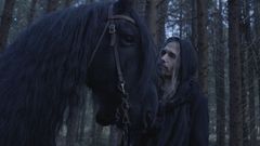 Kuvassa henkilö seisoo metsässä suuren mustan hevosen vieressä.