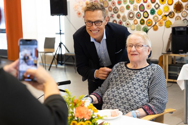 Pian 90-vuotias Eeva Heikkonen poseeraa kahvipöydässä kuvaajilla presidentti Alexander Stubbin kanssa Voutilakeskuksessa Hämeenlinnassa.