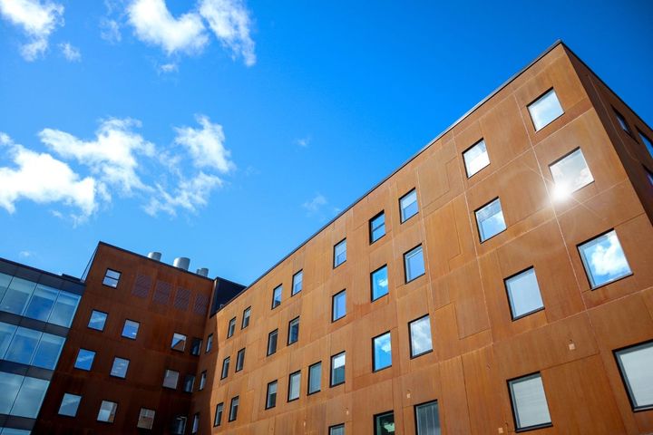 Moderni rakennus, jossa on paljon ikkunoita, kirkasta sinistä taivasta vasten.