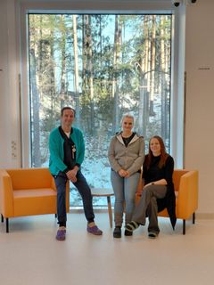 Kolme henkilöä istuu kahdella sohvalla suuren ikkunan edessä. Taustalla näkyy talvinen maisema.