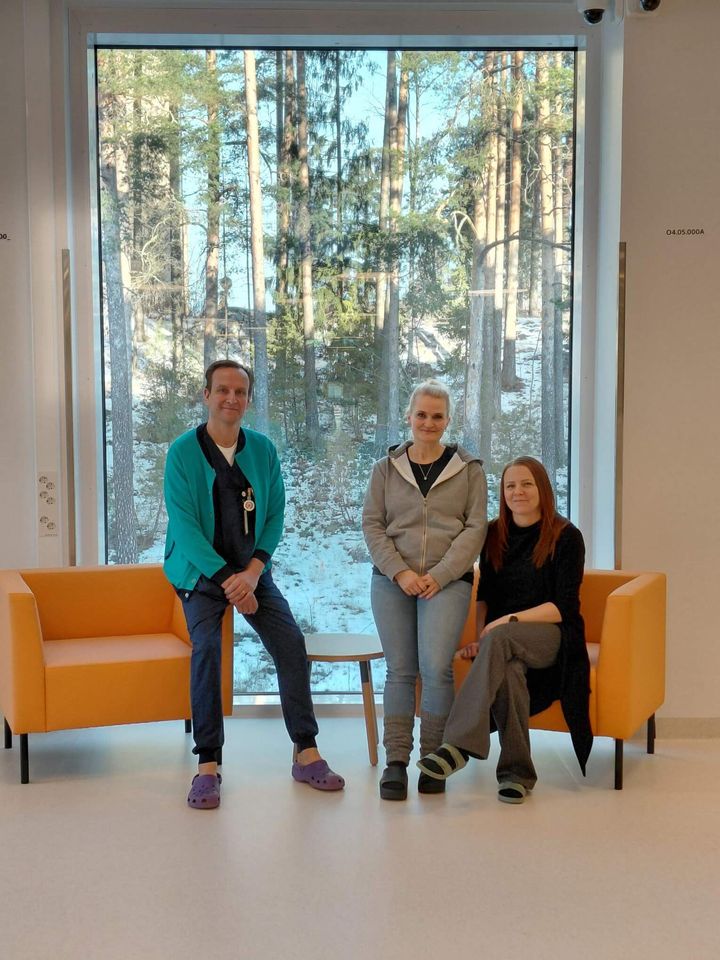 Kolme henkilöä istuu kahdella sohvalla suuren ikkunan edessä. Taustalla näkyy talvinen maisema.