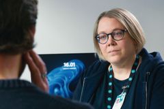 Henkilö istuu pöydän ääressä keskustellen toisen henkilön kanssa tietokoneen äärellä.