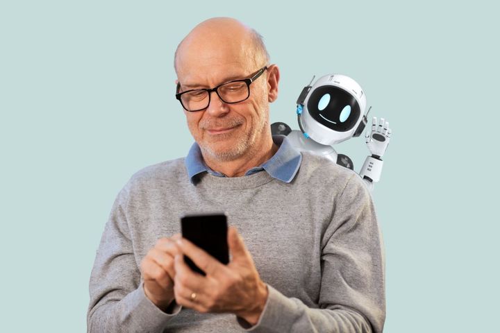Kuvassa vanhempi mies, jolla on älypuhelin kädessään. Pikku robotti kurkistaa olan takaa puhelimeen