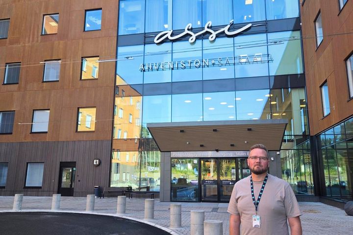 Valokuva: Henkilö seisoo modernin rakennuksen edessä.