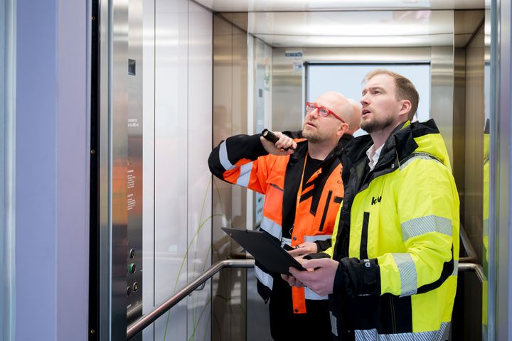 Kaksi henkilöä tarkastelee asiakirjoja hississä.
