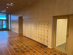 Träkorridor med en skåpsektion och glasdörr till höger. Golvet är gjort av bruna tegelstenar.