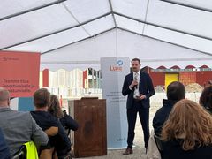 Mies puhumassa teltassa järjestetyssä tilaisuudessa. Taustalla rakennustyömaa.