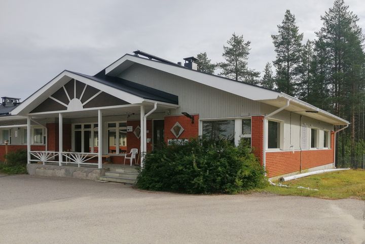 Punatiilinen talo, jossa valkoinen katto ja kuisti, ympärillä metsä.