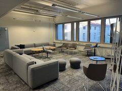 Valoisa toimistotila, jossa on harmaita sohvia, pyöreitä pöytiä ja suuret ikkunat.