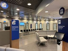 Iso huone, jossa on istuimia ja palvelutiskejä. Seinillä näkyy numeroituja ovia ja kylttejä.
