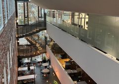 Lasitettu valoaula, jossa näkyy kierreportaat, suuri ikkuna ja kahvilan pöytiä.