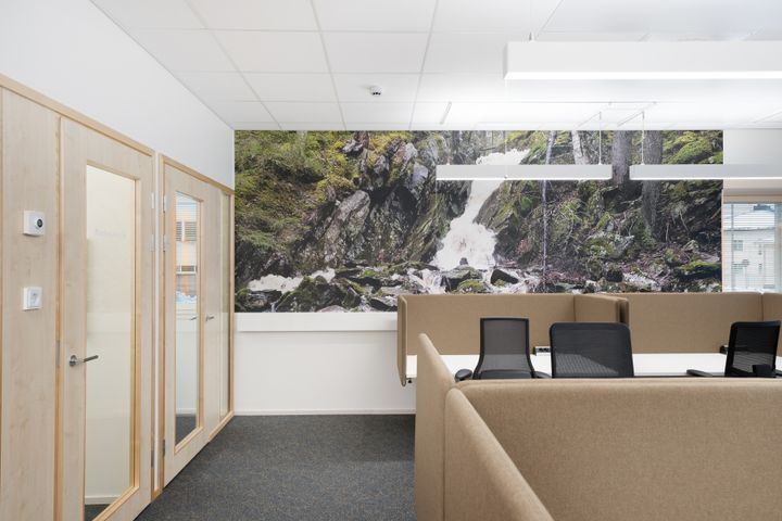 Tytila, jossa on työpöytiä, tuoleja ja luonnonaiheinen seinämaalaus vesiputouksesta.
