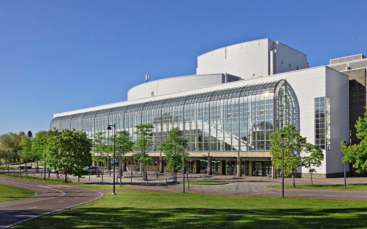 Valkoinen rakennus, jossa on suuri lasijulkisivu, ympäröity vehreällä puistomaisemalla.