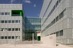 Kuvassa on moderni rakennus, jossa on lasinen sisäänkäynti ja harmaita seinäelementtejä. Rakennuksen yksityiskohdissa on vihreitä korostuksia.