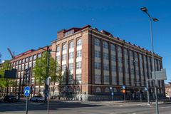 Punatiilinen kerrostalo, jossa on suuria valkoisia ikkunoita. Rakennus sijaitsee kadunkulmassa, ja kuvassa on liikennemerkkejä ja katulamppuja, sekä muutama puu.