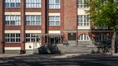 Punatiilisen rakennuksen sisäänkäynti, jossa on katos ja portaat.