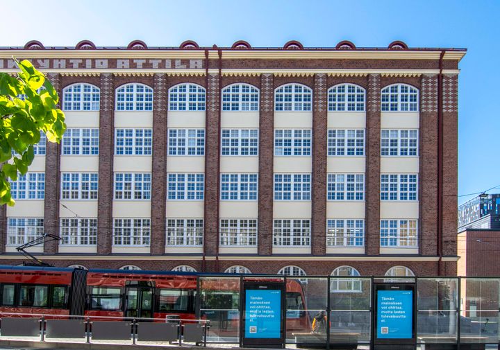 Punatiilinen, suurilla, kaarevilla ikkunoilla varustettu rakennus, edessä kulkee raitiovaunu.