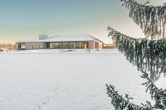 Luminen pelto ja etualalla kuusi. Pellon takana moderni ja vaalea rakennus, jossa laajasti ikkunaseiniä.