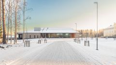 Lumipeitteinen tie johtaa modernille rakennukselle, jota ympäröivät talviset puut. Vaaleassa rakennuksessa laajasti ikkunaseiniä.