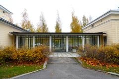 Rakennuksen lasinen sisäänkäynti, jota ympäröivät syksyiset puut ja pensaat.