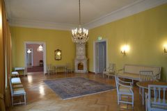 Tyylikäs oleskeluhuone, jossa on keltainen seinä, kattokruunu, vaalea parkettilattia ja valkoisia huonekaluja.