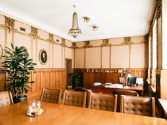 Tyylikkäästi sisustettu toimisto, jossa on puupaneloidut seinät, koristeellisia yksityiskohtia, suuri pöytä ja tuoleja.