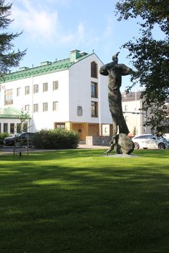 Patsas vehreällä nurmikolla, taustalla valkoinen rakennus.