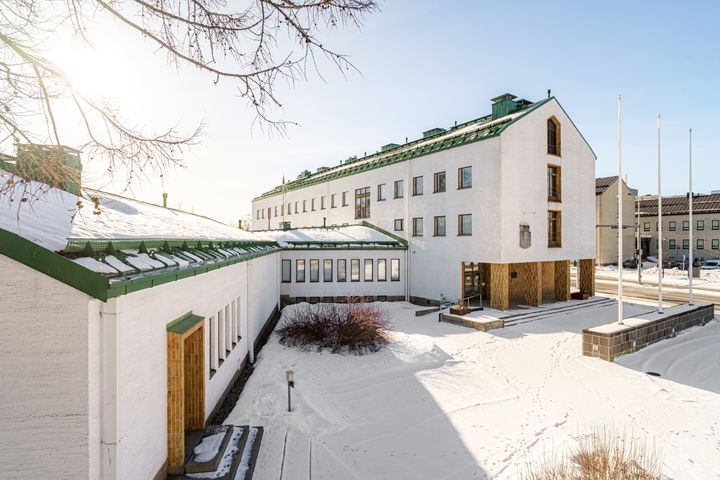 Valkoinen, moderni rakennus lumisessa maisemassa. Aurinko paistaa kirkkaalta taivaalta.